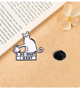 Detail of white enamel cat brooch with I Do What I Want slogan on warm textured desk