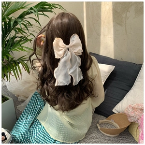 Detail view of a large cream chiffon bow hair clip worn by a model in a bright indoor setting