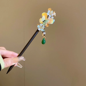 Detail of wooden hairpin featuring a butterfly, flower charm and green jade teardrop tassel