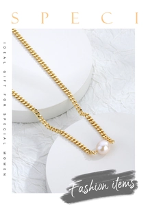 Detail view of gold Cuban chain necklace with a round white freshwater pearl on white props