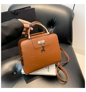 Détail d'un sac en cuir crocodile marron avec poignée en métal et pendentif cerf