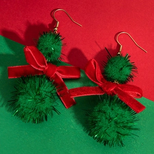Macro detail of Christmas earrings with green pom-poms and a red velvet bow
