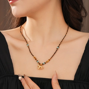 Detail of vintage beaded necklace with tiger eye stones and golden rocking horse pendant