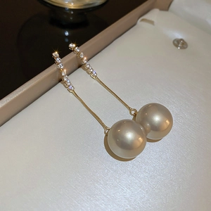 Macro shot of long gold chain earrings with sparkling diamonds and large pearl pendants