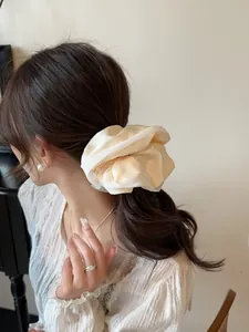 Detail of elegant cream satin scrunchie with soft silk texture on a model