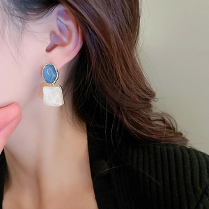 Close-up of geometric earrings with blue and pearl squares on a female model