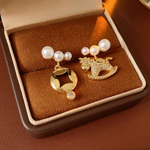 Détail de boucles d'oreilles cheval asymétriques dorées avec perles et cristaux