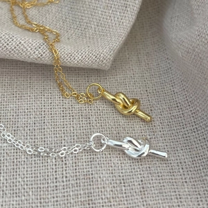 Detailed view of silver and gold knot necklaces on textured linen fabric background