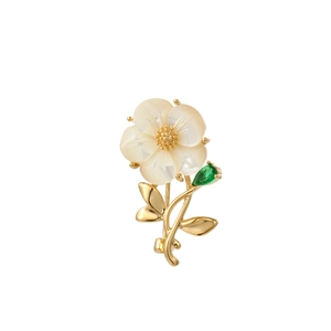 Detail of elegant shell flower brooch with golden leaf and green teardrop gemstone
