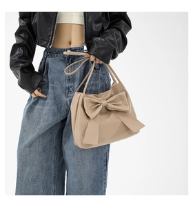 Detail of a khaki tote bag with a large bow decoration and minimalist leather texture