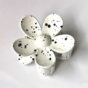 Detailopname van witte bloem haarclip met artistiek zwart inktspatpatroon