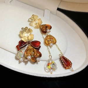 Détail de boucles d'oreilles fleurs dorées asymétriques avec cœurs en résine ambrée