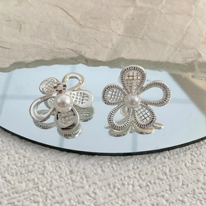 Detailed view of silver hollow flower earrings with white pearls on a mirror