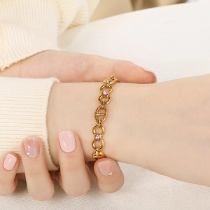 Detail of gold-plated bracelet with pink zircon stones worn on wrist against white background