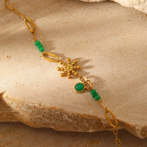 Detail of gold chain bracelet with green stones and sun pendant on a natural stone