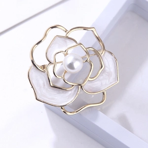 Detailed view of white camellia brooch with gold trim and pearl on jewelry box