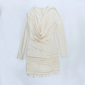 Détail de robe crème à manches longues avec décolleté drapé et ourlet froncé sur le côté
