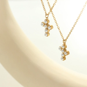 Elegant gold cross necklace featuring faux pearls on a minimalist off-white display stand