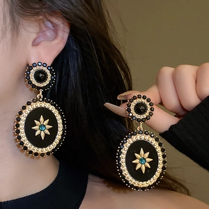 Close-up of vintage black and gold earrings with green gemstones worn by a model