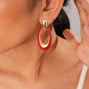 Close-up of a model wearing a gold and red enamel oval drop earring with a polished finish