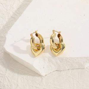 Close-up of golden hoop earrings with heart pendants on a white textured stone base