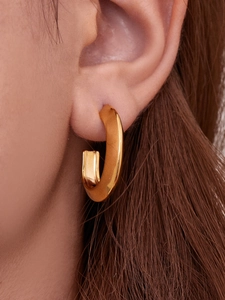 Close-up of chunky gold U-shaped earring with a polished mirror finish on ear
