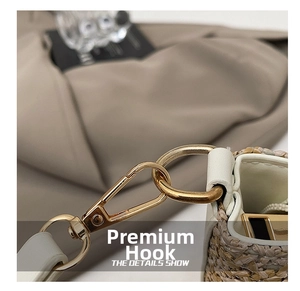Close-up of golden metal hook on straw bucket bag with white leather trim detail