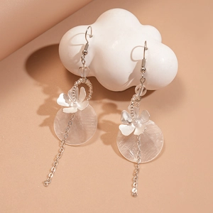 Floral shell drop earrings with beads and metallic tassels on a white cloud prop