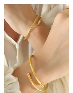 Detail of two gold cable-style open bracelets with cylindrical ends on a model's wrist