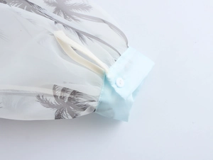 Dettaglio del polsino della camicia in organza con stampa a palma e orlo azzurro a bottoni