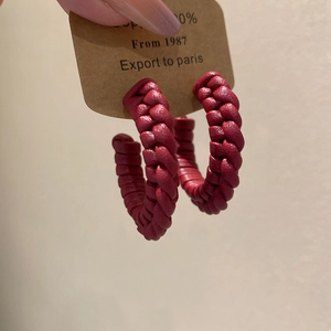 Detail of dark red woven leather C-shaped earrings with intricate handmade texture