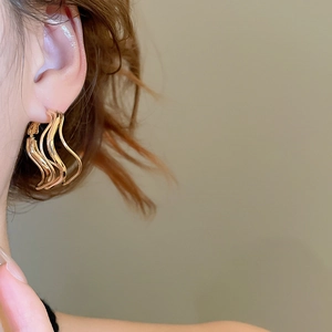 Detail shot of wavy gold multi-layered hoop earrings worn by a model on a beige background