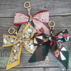 Three camellia silk scarf bow keychains with various floral patterns on wooden surface