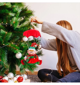 Hanging a red Christmas parachute elf doll decoration on a festive tree at home
