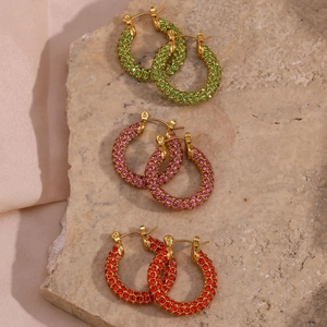 Macro detail of three multi-color zircon hoop earrings on a pink silk background