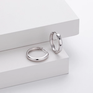 Macro detail of polished s925 silver hoop earrings on minimalist white geometric props