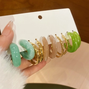 Détail de cinq paires de boucles d'oreilles en acrylique en C, tons vert, beige et or