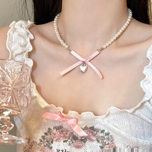 Detail of pink silk bow and heart pendant on a white pearl necklace worn by a model