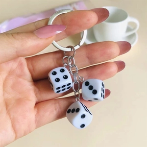 Close-up of a silver keychain featuring three white resin dice pendants with black dots