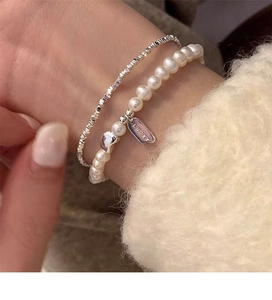 Detail of layered S925 silver lucky charm pearl bracelet and textured silver bead chain