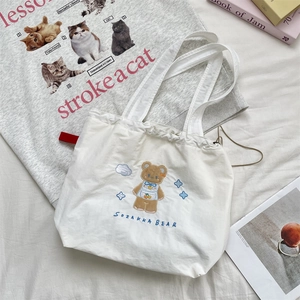 Detail of cute brown bear embroidery and drawstring closure on a white canvas tote bag
