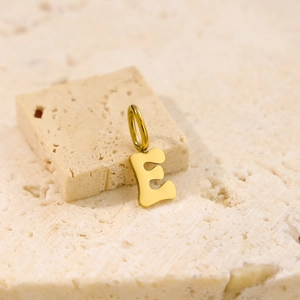 Macro shot of a polished golden letter E pendant on a textured beige stone surface