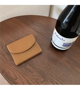 Top view of a minimalist brown leather card holder on a wooden table with a wine bottle