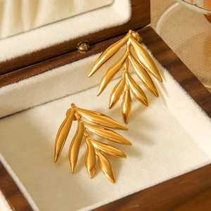Close-up of 18K gold leaf-shaped stainless steel earrings on a beige velvet jewelry box