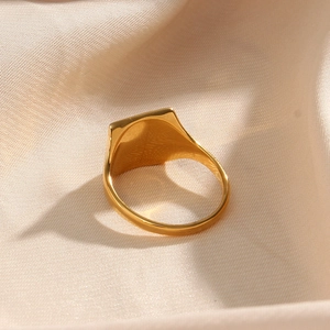 Detailed view of a gold square signet ring with white zircon on beige silk fabric