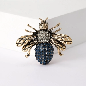 Macro view of a gold bee brooch featuring intricate blue and clear rhinestone detailing
