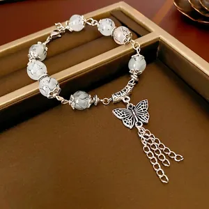 Bracelet perlé élégant avec pendentif papillon et pompons métalliques sur plateau