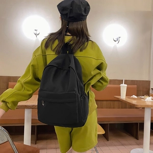 Minimalist large black nylon backpack shown on model in a stylish cafe setting
