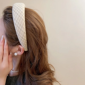Dettaglio del cerchietto in tessuto a quadri beige abbinato a eleganti gioielli di perle