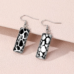 Rectangle cow print drop earrings with silver metal base on pink textured background